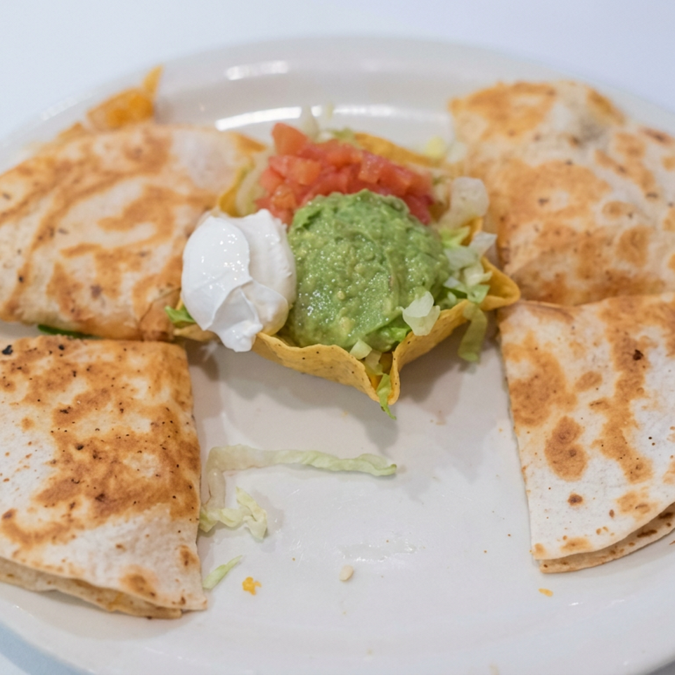 Plate of toasted quesadilla wedges surrounding guacamole, sour cream, salsa, lettuce, and tortilla chips.