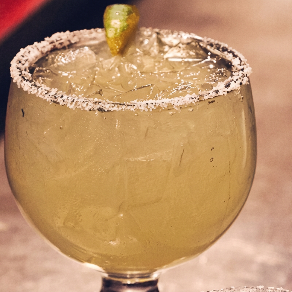 Golden margarita with ice, a salted rim, and lime garnish served in a round stemmed glass.